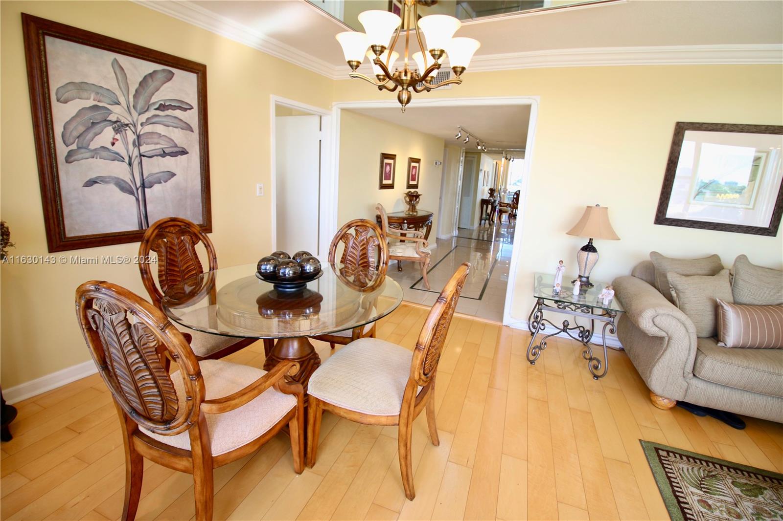 A dining area with a glass table and wooden chairs sits beside a living room — 900 Bay Dr # 319, Miami Beach FL 33141, MIAMI BEACH, FL