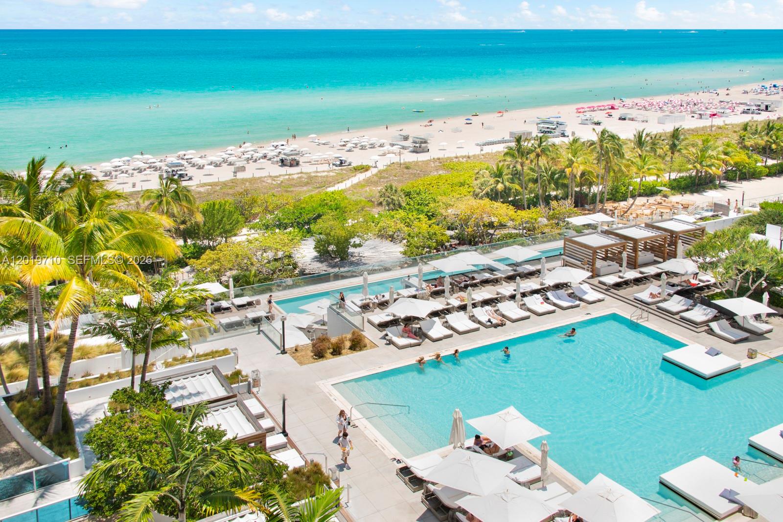 An elevated view of a resort pool deck with lounge chairs overlooking a sandy beach — 102 24th St # 1012, Miami Beach FL 33139, MIAMI BEACH, FL