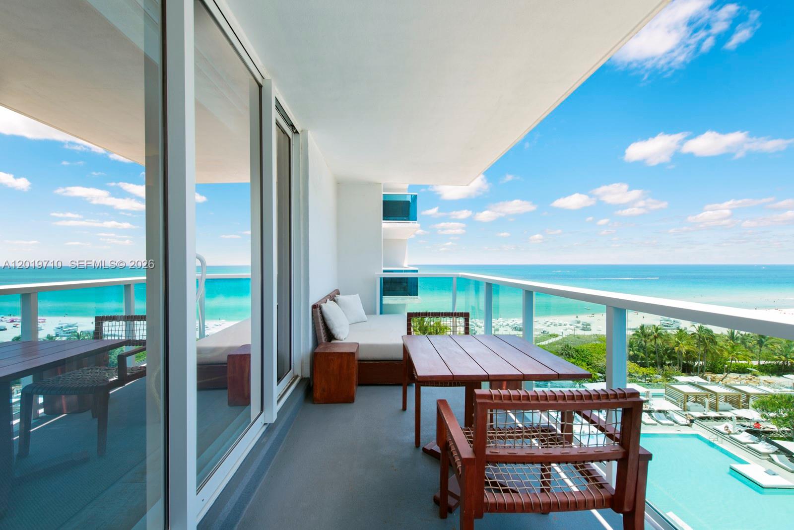 A balcony features a wooden table, chairs, and a daybed overlooking the ocean and pool — 102 24th St # 1012, Miami Beach FL 33139, MIAMI BEACH, FL