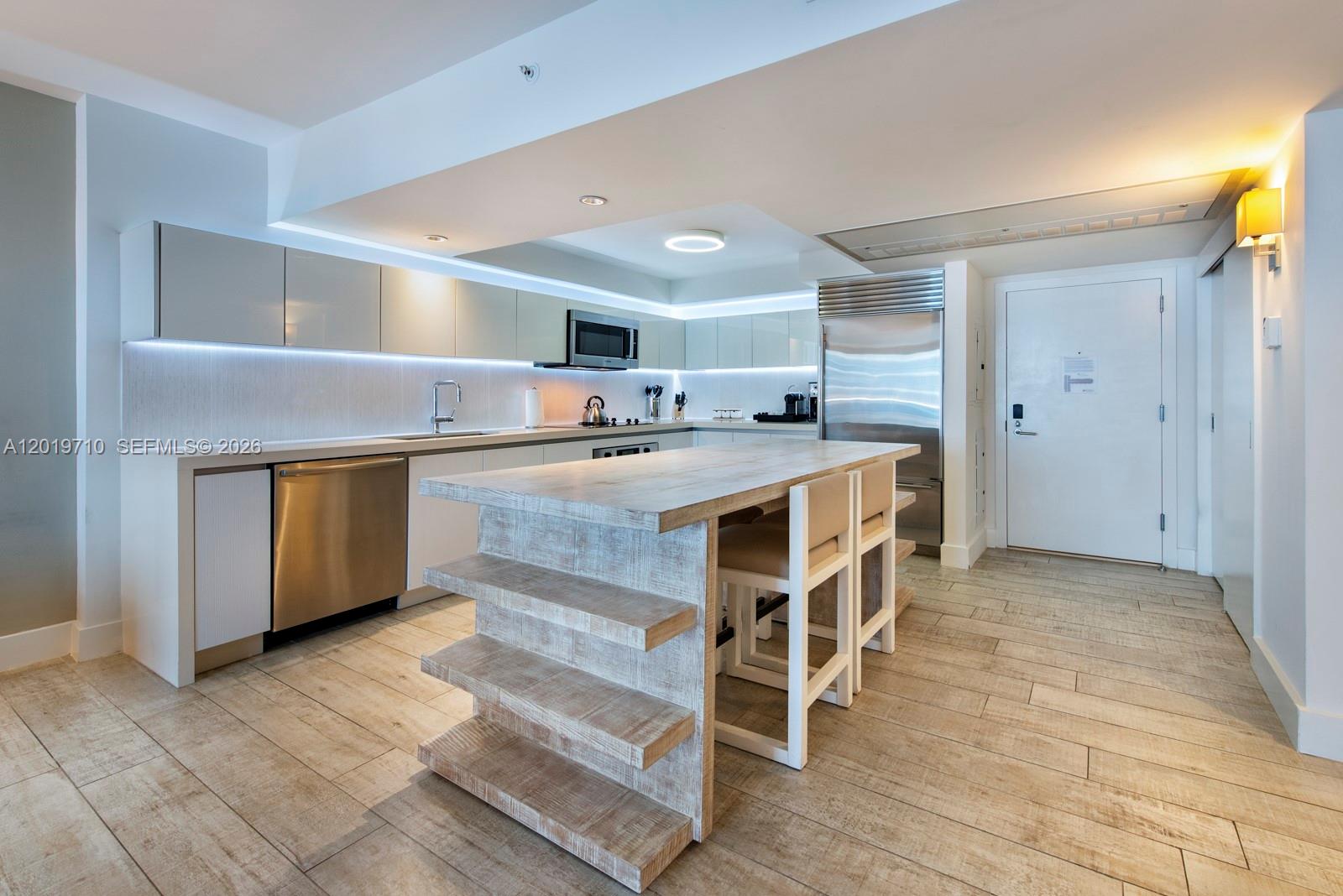 A modern kitchen features light wood-look tile floors, white cabinetry, and a rustic wooden island — 102 24th St # 1012, Miami Beach FL 33139, MIAMI BEACH, FL