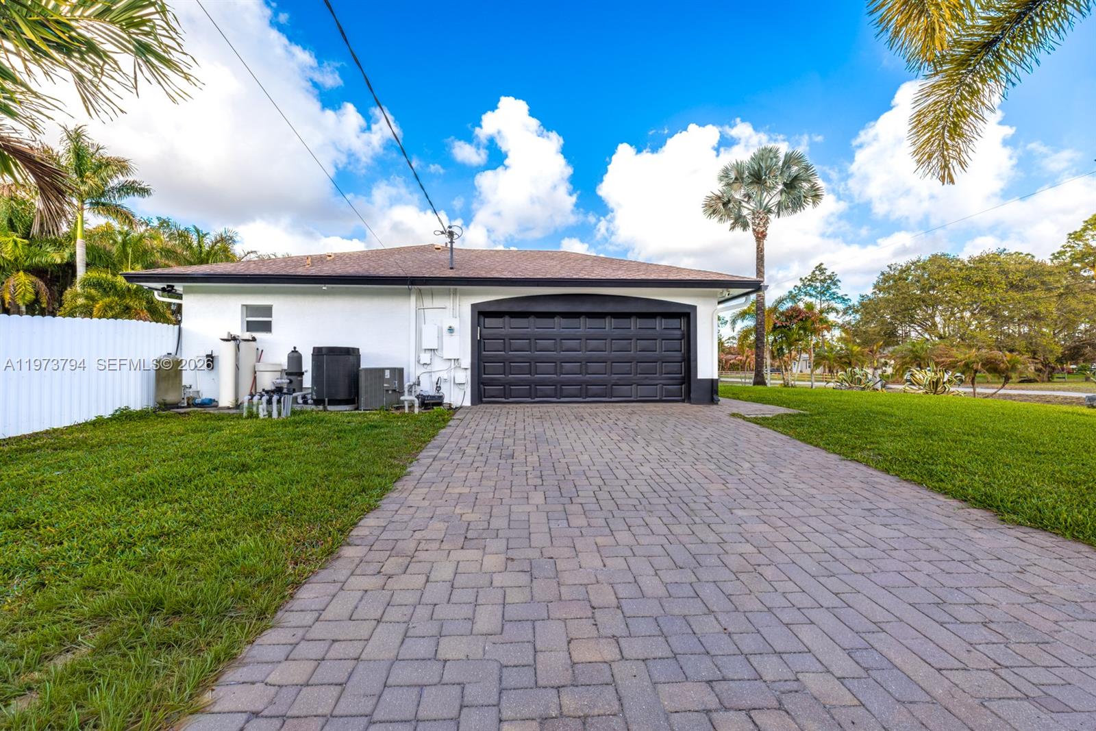 A white house with a black garage door and a paved driveway sits on a lawn — 15780 N 75th Ln N, Loxahatchee FL 33470, LOXAHATCHEE, FL