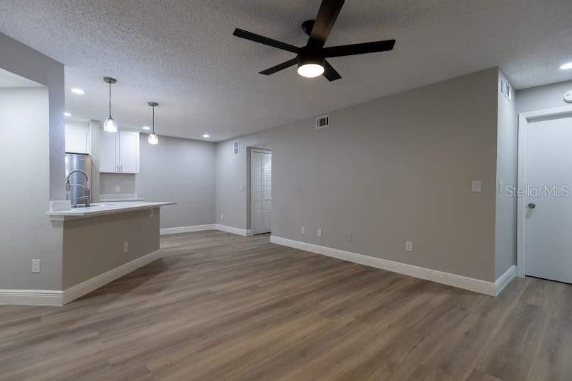 An open-concept living area features light wood-look flooring, gray walls, a ceiling fan, and a kitchen — 4572 COMMANDER DRIVE UNIT 1212, ORLANDO, FL