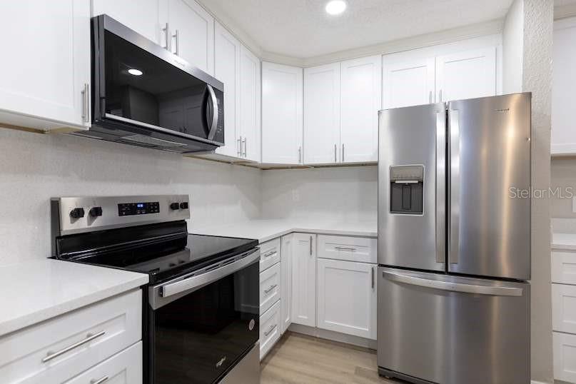 A kitchen features white cabinets, stainless steel appliances, and light-colored countertops — 4572 COMMANDER DRIVE UNIT 1212, ORLANDO, FL