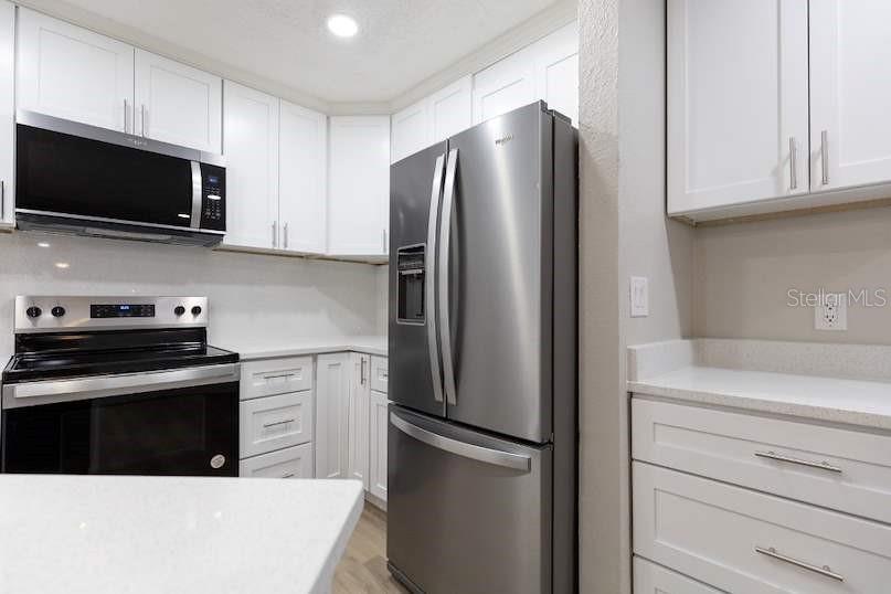 A kitchen with white cabinets, stainless steel appliances, and light-colored countertops — 4572 COMMANDER DRIVE UNIT 1212, ORLANDO, FL