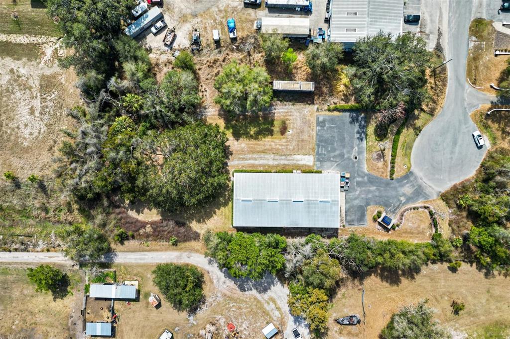 An aerial view shows a rectangular metal building surrounded by trees, parking, and rural land — 118 WEBER AVENUE, LEESBURG, FL