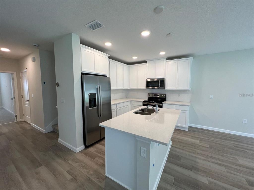 A modern kitchen features white cabinetry, stainless steel appliances, a center island, and wood-look flooring — 2779 NARCOOSSEE COMMONS WAY, ST CLOUD, FL