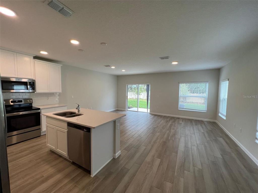A kitchen with white cabinets and a center island opens into a spacious living area — 2779 NARCOOSSEE COMMONS WAY, ST CLOUD, FL