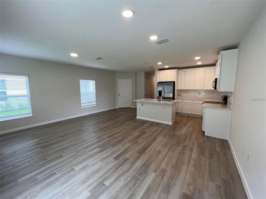 An open-concept kitchen and living area features light wood-look flooring and white cabinetry — 2779 NARCOOSSEE COMMONS WAY, ST CLOUD, FL