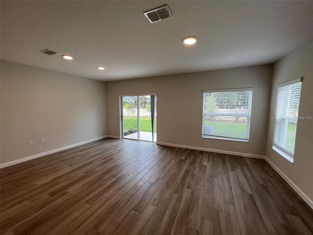 An empty living room features light-colored walls, wood-look tile flooring, recessed lighting, and sliding doors — 2779 NARCOOSSEE COMMONS WAY, ST CLOUD, FL