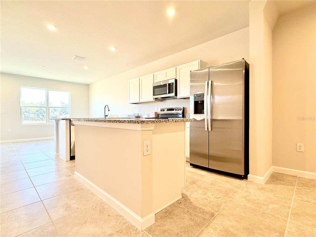 A kitchen features a granite-topped island, white cabinetry, and stainless steel appliances on tile flooring — 1188 PORT BLUE WAY, LADY LAKE, FL
