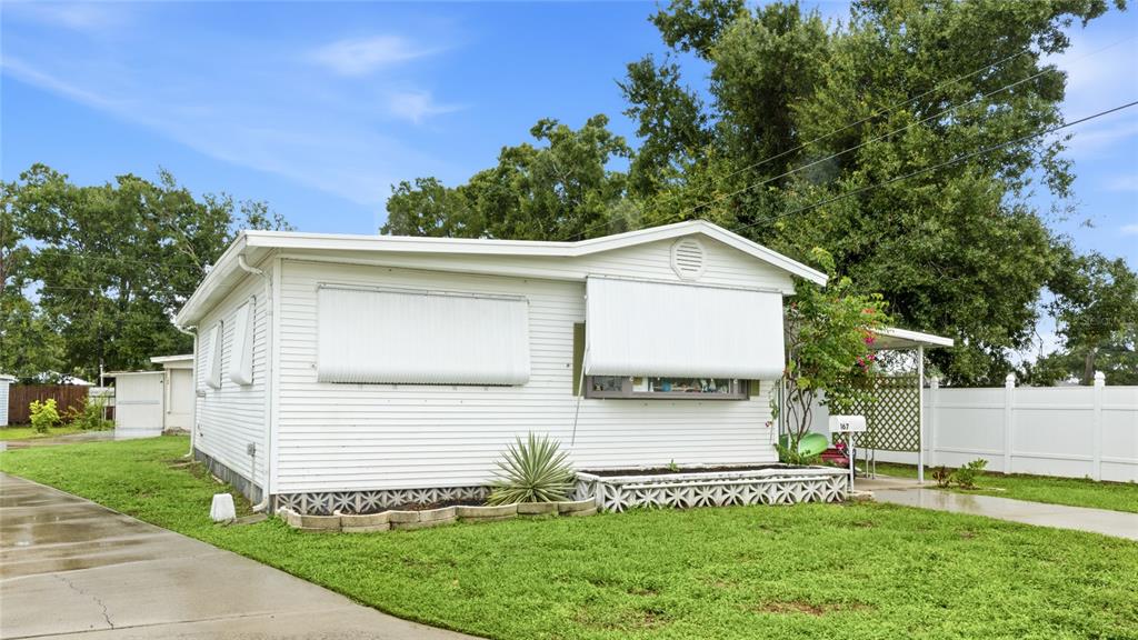 A white mobile home with metal window awnings and a concrete driveway sits on grass — 1891 ENGLEWOOD ROAD UNIT 167, ENGLEWOOD, FL