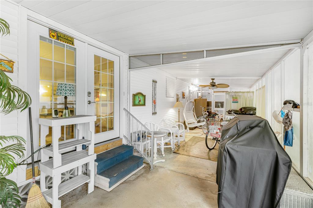A covered outdoor patio features a white door, blue steps, a grill, and patio furniture — 1891 ENGLEWOOD ROAD UNIT 167, ENGLEWOOD, FL