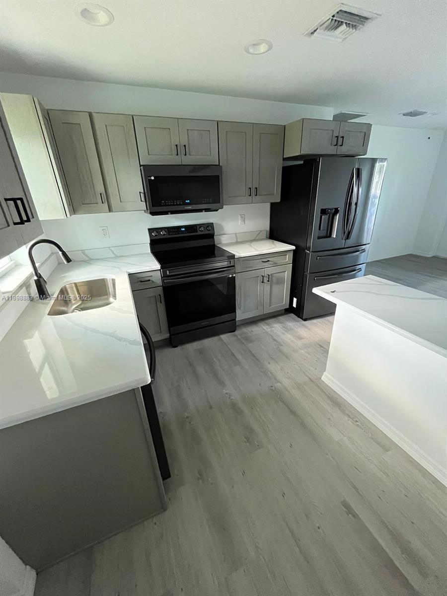 A kitchen features gray cabinets, black appliances, white countertops, and light wood-look flooring — 5218 SE 43 St, Okeechobee FL 34974, OKEECHOBEE, FL