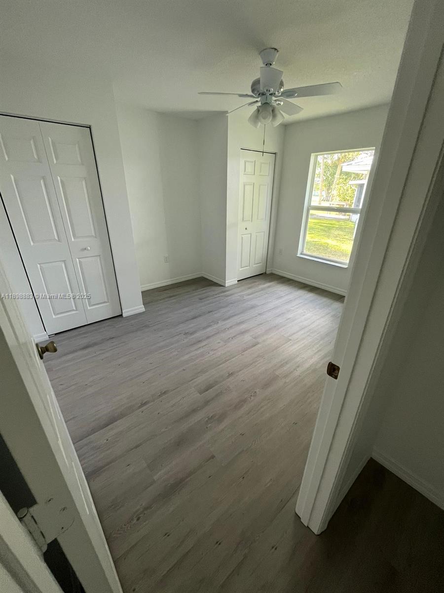 A bedroom features light wood-look flooring, white walls, two closet doors, and a ceiling fan — 5218 SE 43 St, Okeechobee FL 34974, OKEECHOBEE, FL