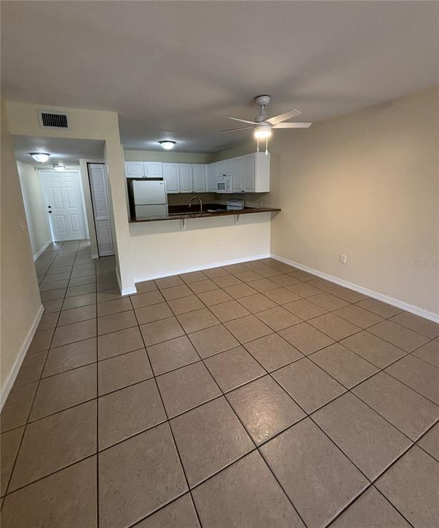 A kitchen with white cabinets and a breakfast bar overlooks a tiled living area — 25050 SANDHILL BOULEVARD UNIT 1A3, PUNTA GORDA, FL