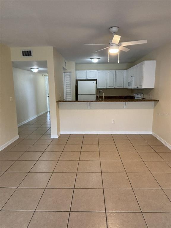 A kitchen with white cabinets and a breakfast bar overlooks a tiled living area — 25050 SANDHILL BOULEVARD UNIT 1A3, PUNTA GORDA, FL
