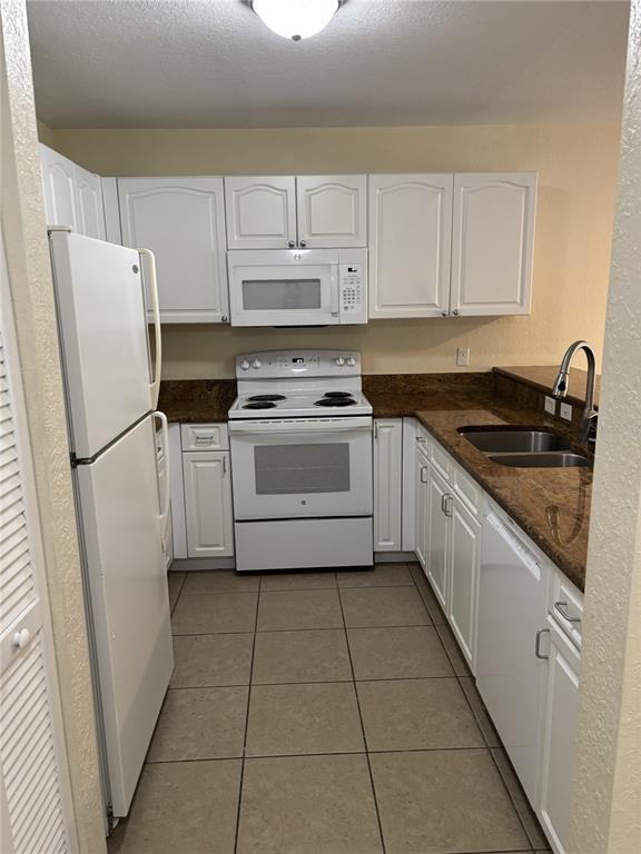 A galley kitchen features white cabinets, white appliances, and brown granite countertops — 25050 SANDHILL BOULEVARD UNIT 1A3, PUNTA GORDA, FL