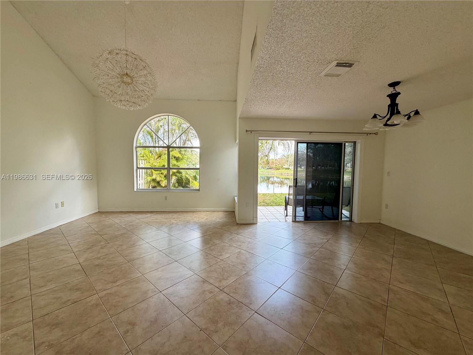 A bright living room features tile flooring, vaulted ceilings, a large arched window, and sliding doors — 12619 NW 11th Pl, Sunrise FL 33323, SUNRISE, FL