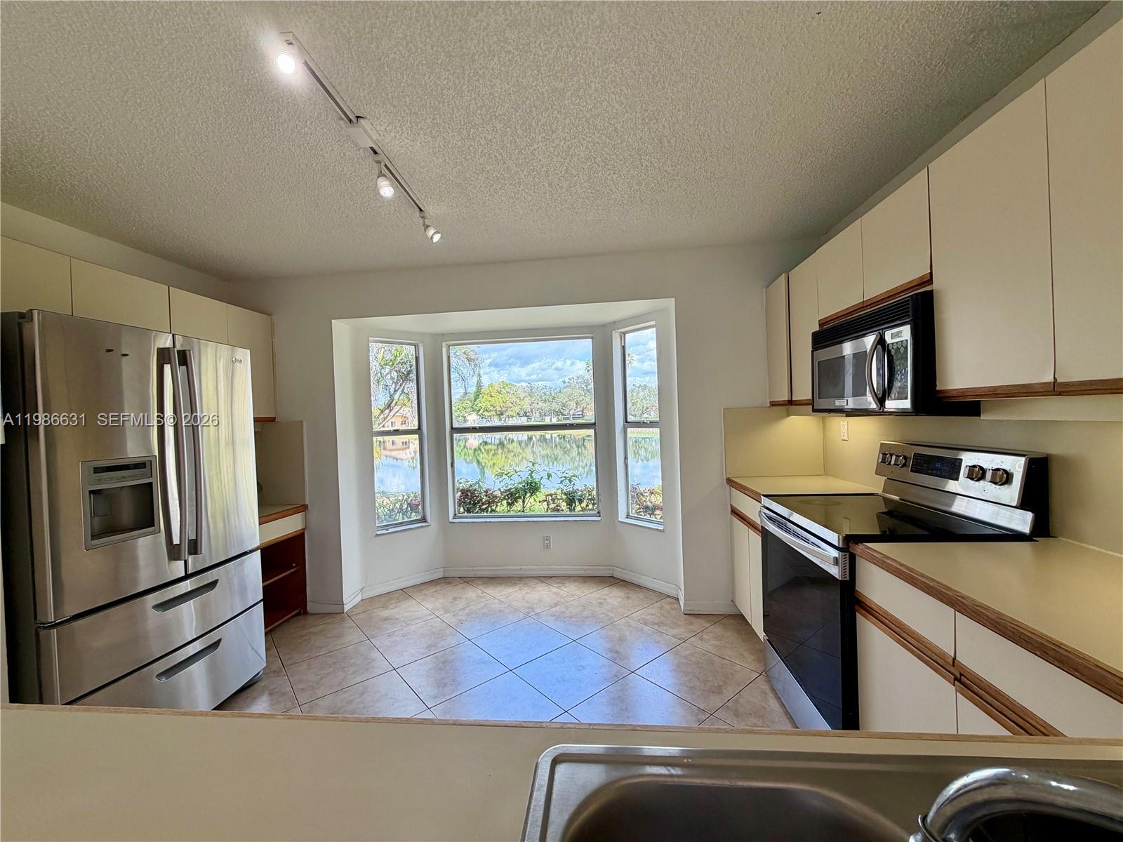 A kitchen features stainless steel appliances, white cabinets, tile floors, and a bay window view — 12619 NW 11th Pl, Sunrise FL 33323, SUNRISE, FL