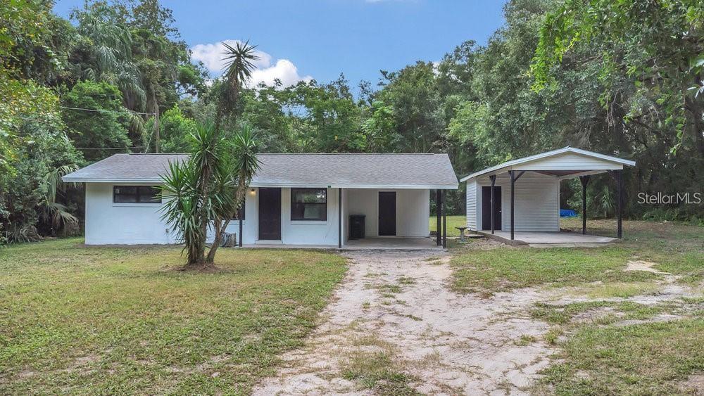 A single-story white house with a covered carport sits on a grassy, wooded lot — 700 WEST CHURCH AVENUE, LONGWOOD, FL