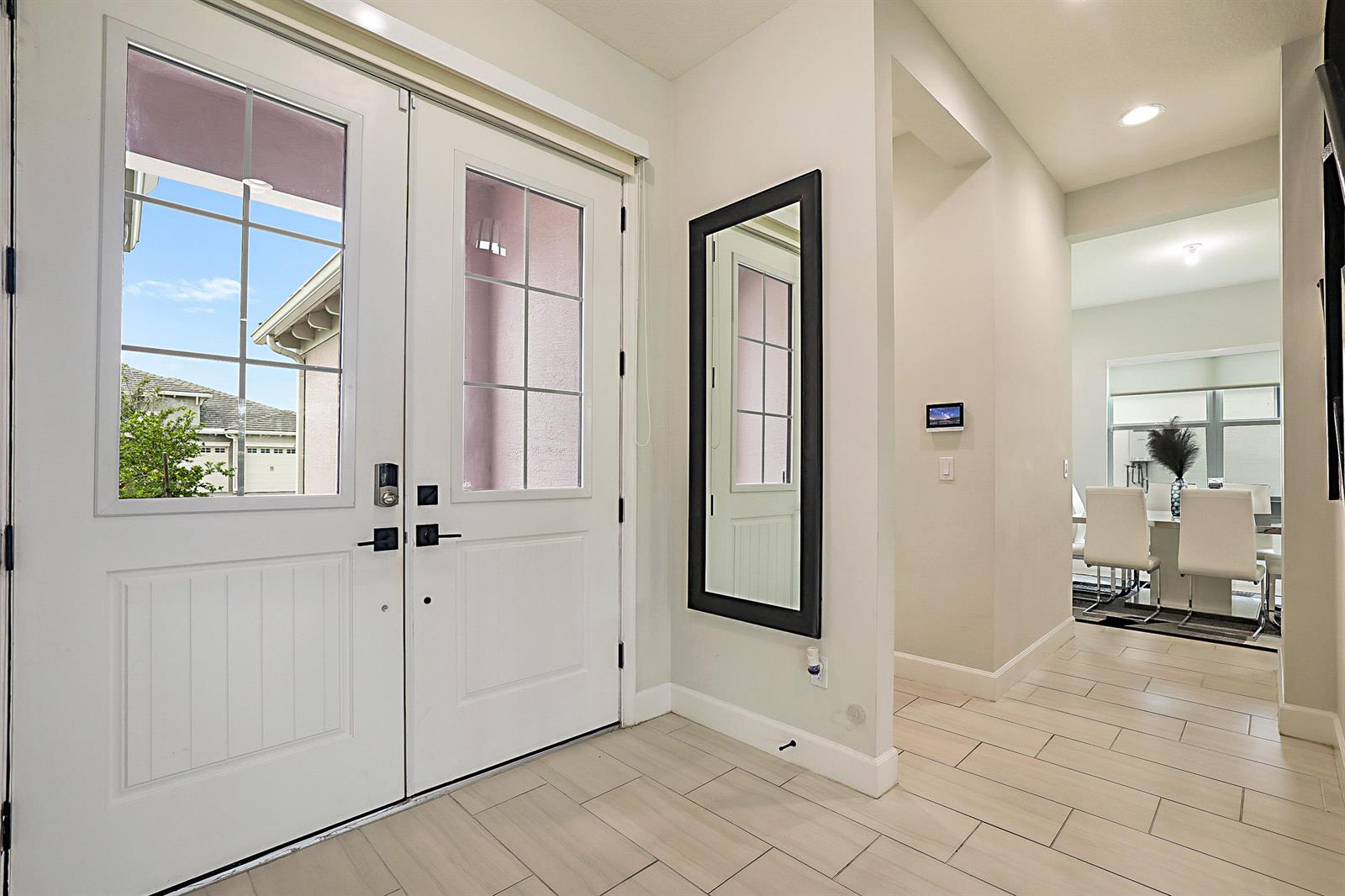 An entryway features white double doors, a black-framed mirror, and light-colored tile flooring — 16088 Orchard Drive, FL 33470, FL
