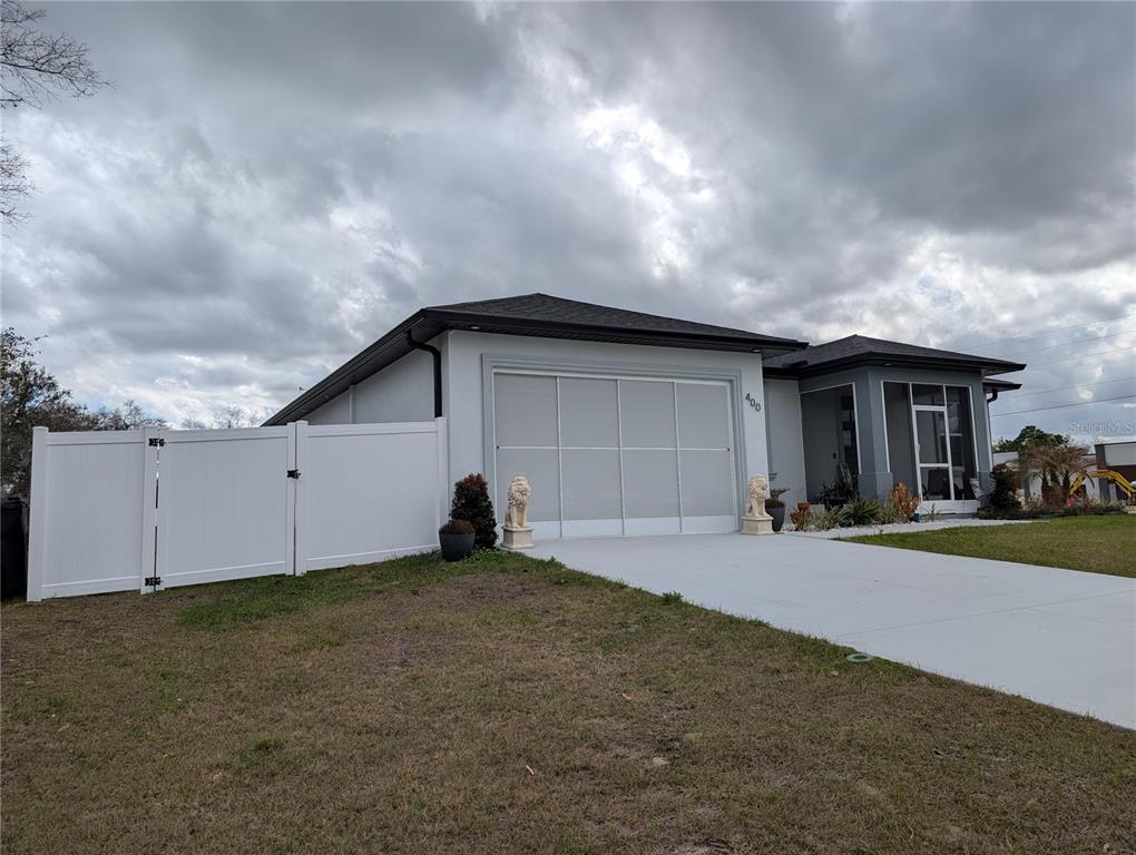 A single-story house with a white garage door, a concrete driveway, and a white fence — 400 MIAMI WAY, POINCIANA, FL