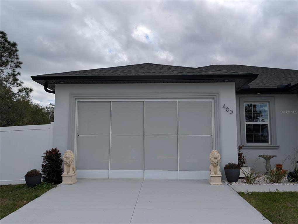 A gray house exterior features a garage with a sliding screen door and lion statues — 400 MIAMI WAY, POINCIANA, FL