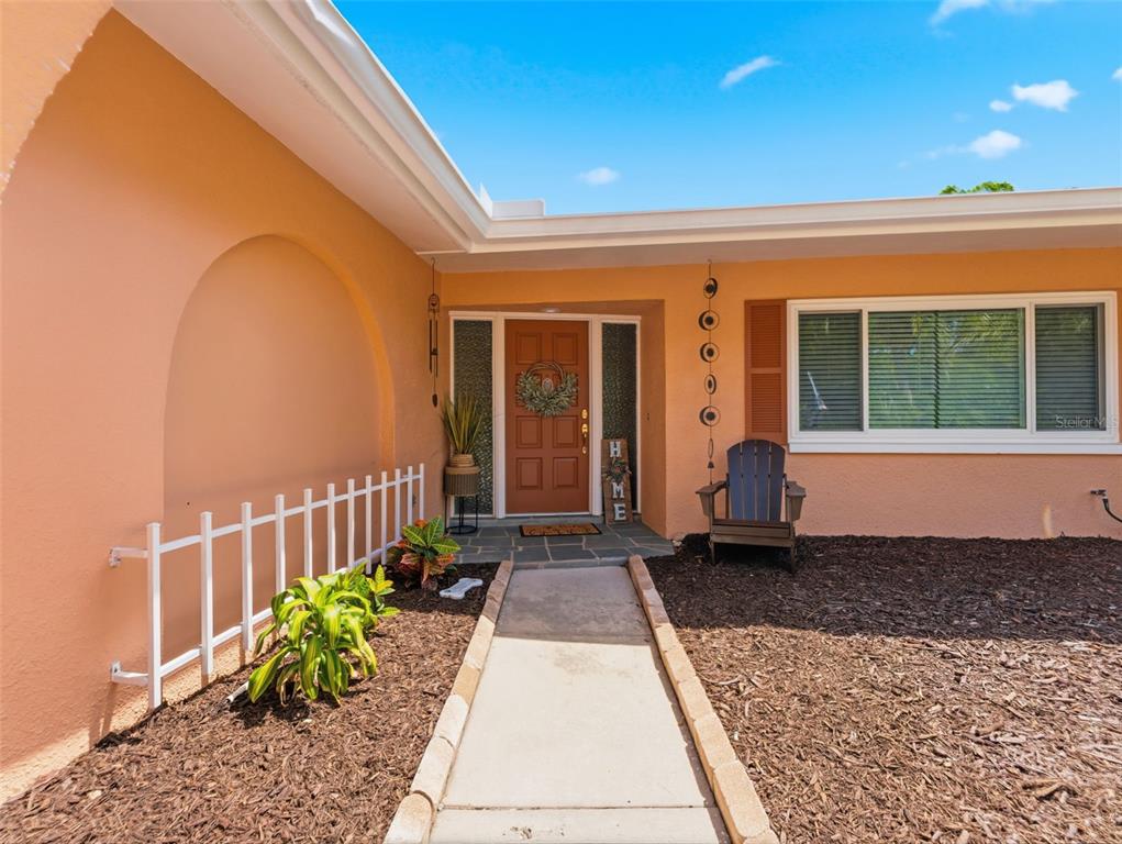 A concrete walkway leads to the front entrance of a peach-colored house with a brown door — 3325 SAN MATEO STREET, CLEARWATER, FL