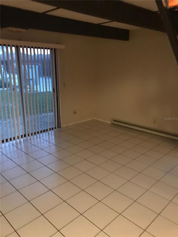A room with white tile flooring, a sliding glass door, and exposed ceiling beams — 3412 OVERLOOK DRIVE, PALM BAY, FL