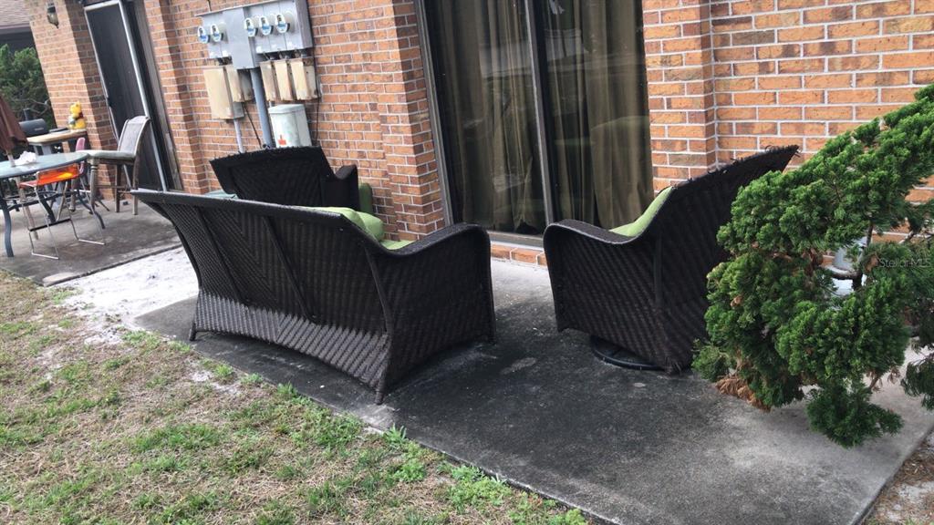 A patio features dark wicker outdoor furniture on a concrete slab against a brick wall — 3412 OVERLOOK DRIVE, PALM BAY, FL
