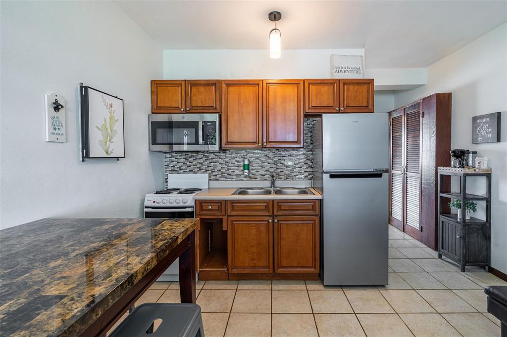 A kitchen features wood cabinets, stainless steel appliances, a tiled backsplash, and a dining table — SR 301 km 11.0 CONDOMINIO PLAYAS DEL CARIBE RESORT UNIT 303 - D, CABO ROJO, PR