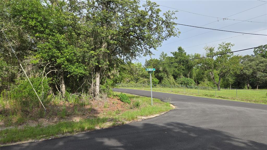 A paved road curves past a street sign and a wooded lot with a chain-link fence — 4771 N REDWOOD AVENUE, HERNANDO, FL