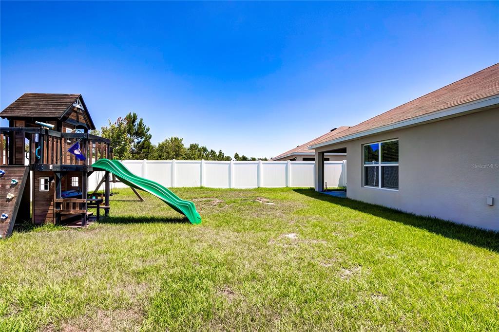 A backyard features a wooden playset with a green slide next to a house exterior — 4111 AUTUMN AMBER DRIVE, SPRING HILL, FL