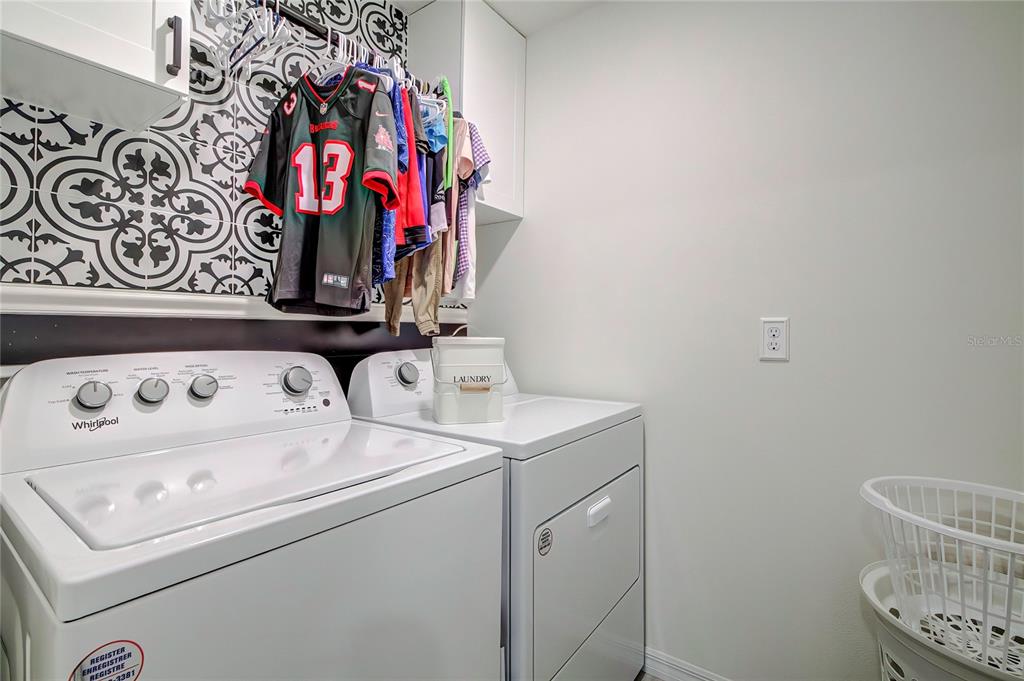 A laundry room features white appliances, a patterned tile backsplash, and a hanging clothes rack — 4111 AUTUMN AMBER DRIVE, SPRING HILL, FL