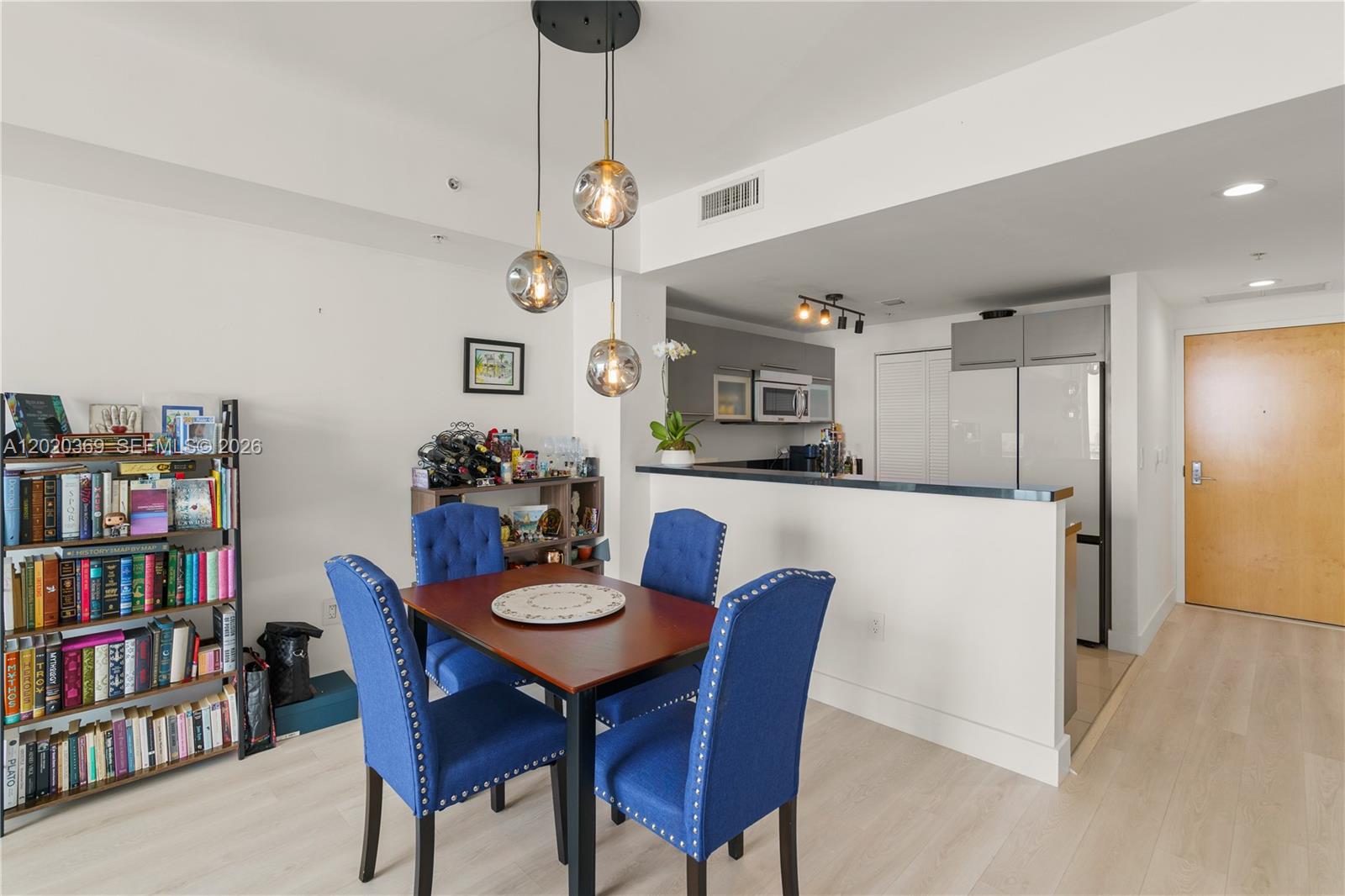 A dining area features a wooden table with blue chairs beneath three glass pendant lights — 253 NE 2nd St # 2003, Miami FL 33132, MIAMI, FL