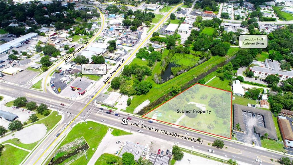 An aerial view shows a vacant, grass-covered lot outlined in red along a busy road — 3223 14TH STREET W, BRADENTON, FL