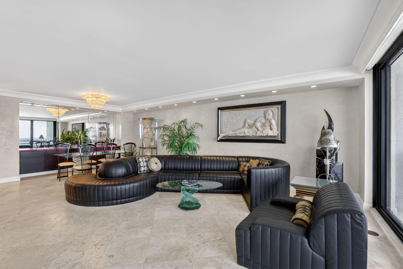A spacious living room features a large black curved sofa, tile floors, and wall art — 1400 S Ocean Boulevard # 1003, Boca Raton FL 33432, BOCA RATON, FL