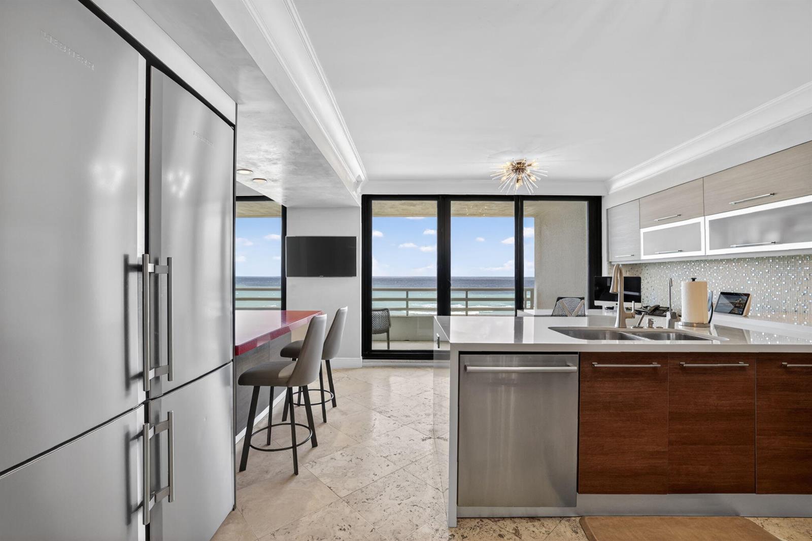 A modern kitchen features stainless steel appliances, a breakfast bar, and ocean views through balcony doors — 1400 S Ocean Boulevard # 1003, Boca Raton FL 33432, BOCA RATON, FL