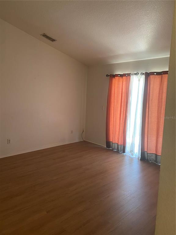 An empty room features light wood-look flooring, white walls, and orange curtains over a window — 135 STEWART LAKE LOOP, GROVELAND, FL