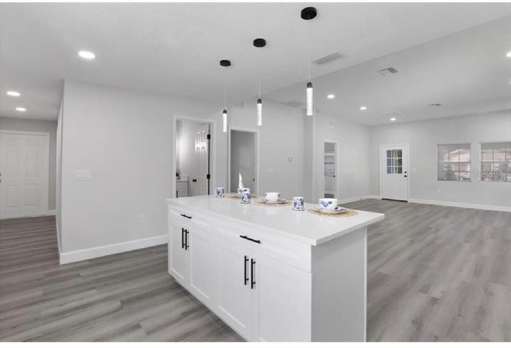 A white kitchen island with pendant lights sits in an open-concept room with gray flooring — 506 N WARNELL STREET, PLANT CITY, FL