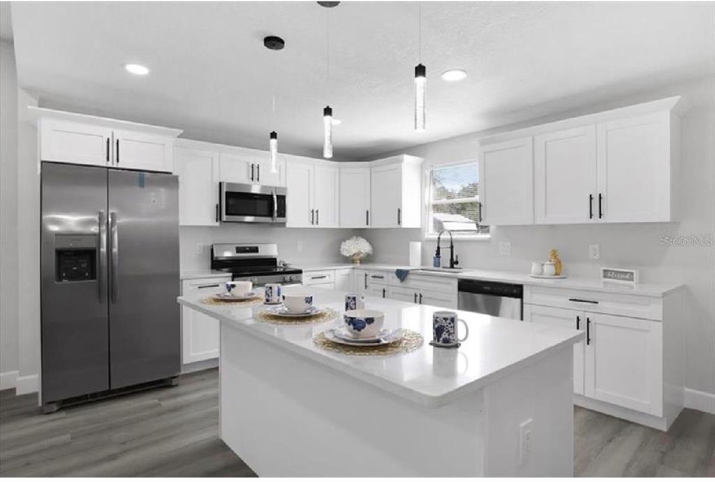 A modern kitchen features white cabinets, stainless steel appliances, a center island, and gray flooring — 506 N WARNELL STREET, PLANT CITY, FL