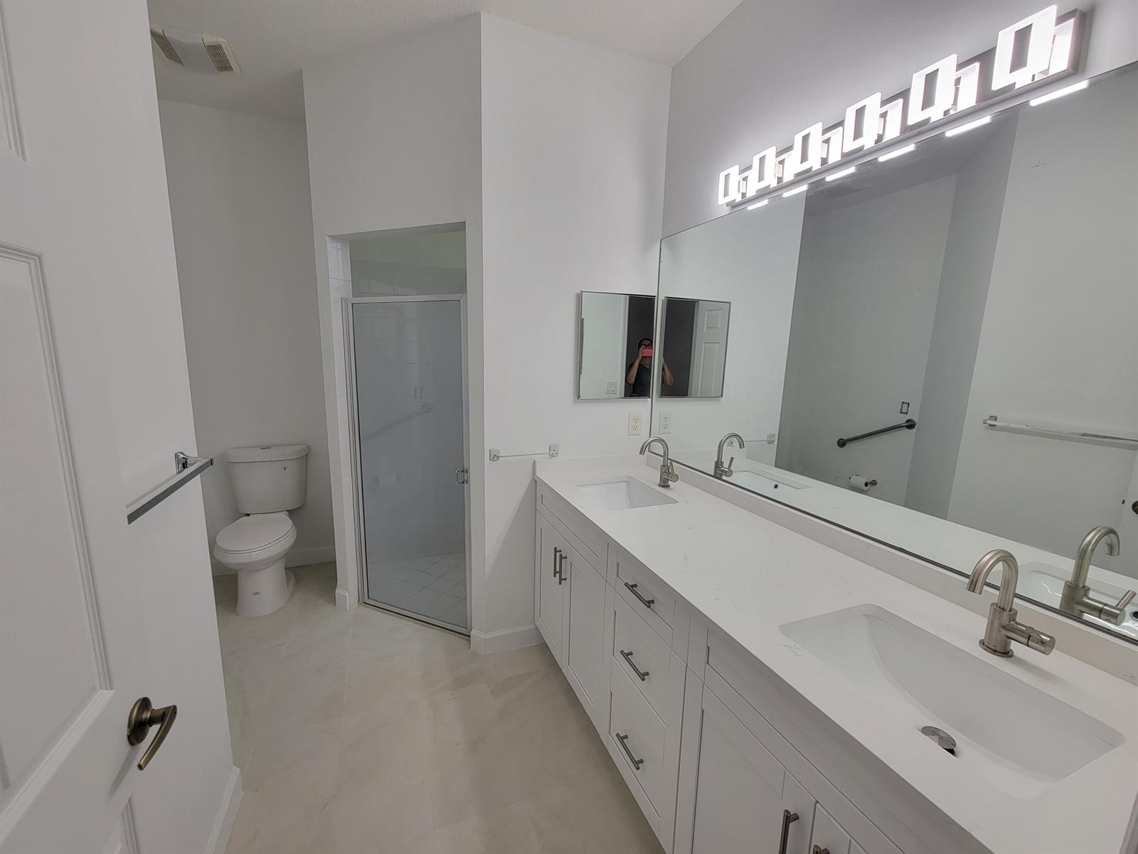 A bright bathroom features a double vanity with white cabinets, quartz countertops, and a large mirror — 3103 Anthem Way, Vero Beach FL 32966, VERO BEACH, FL