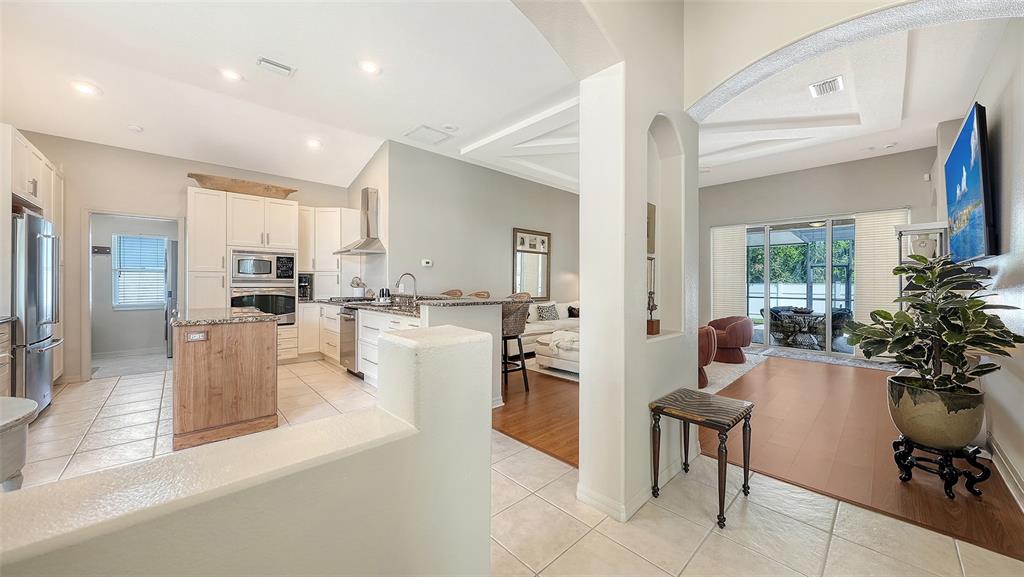 A kitchen with white cabinetry and a wood-toned island opens into a living area — 5122 CREEKSIDE TRAIL, SARASOTA, FL