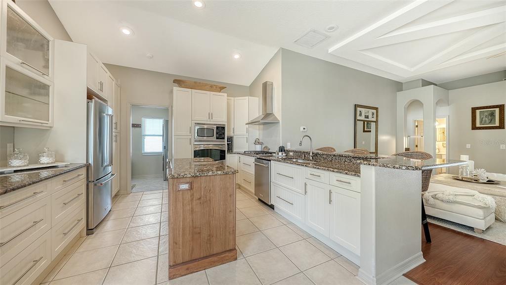 A kitchen features white cabinetry, granite countertops, a wood-toned island, and stainless steel appliances — 5122 CREEKSIDE TRAIL, SARASOTA, FL