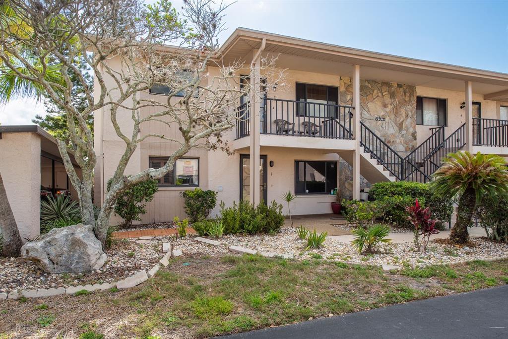 A two-story apartment building exterior with a stone accent wall, balcony, and landscaped front yard — 9910 EAGLES POINT CIRCLE UNIT 3, PORT RICHEY, FL