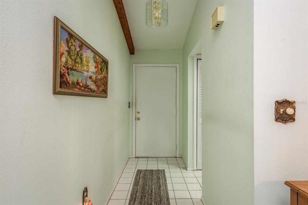 An entryway features white tile flooring, a light green wall, and a wooden ceiling beam — 9910 EAGLES POINT CIRCLE UNIT 3, PORT RICHEY, FL