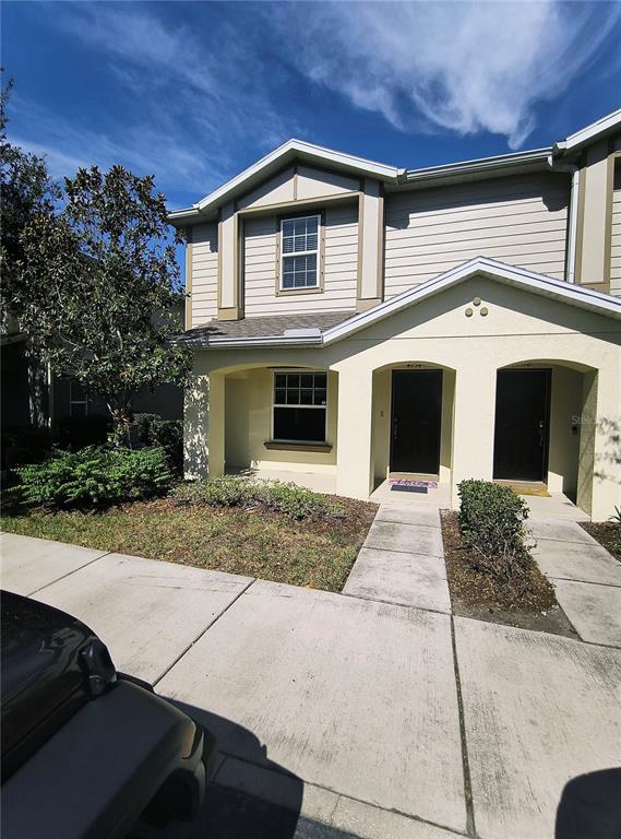 A two-story townhouse exterior features beige siding, stucco walls, and two dark front doors — 4754 CHATTERTON WAY, RIVERVIEW, FL