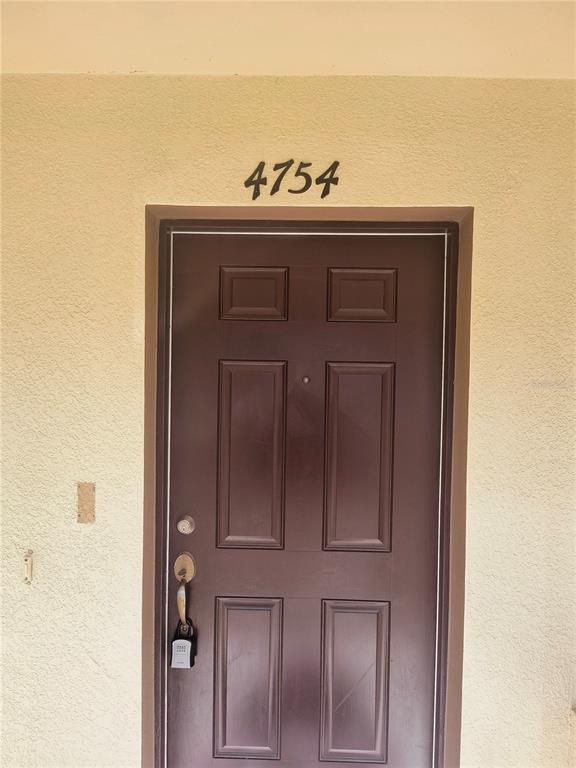A dark brown front door with a lockbox is set into a light-colored stucco wall — 4754 CHATTERTON WAY, RIVERVIEW, FL