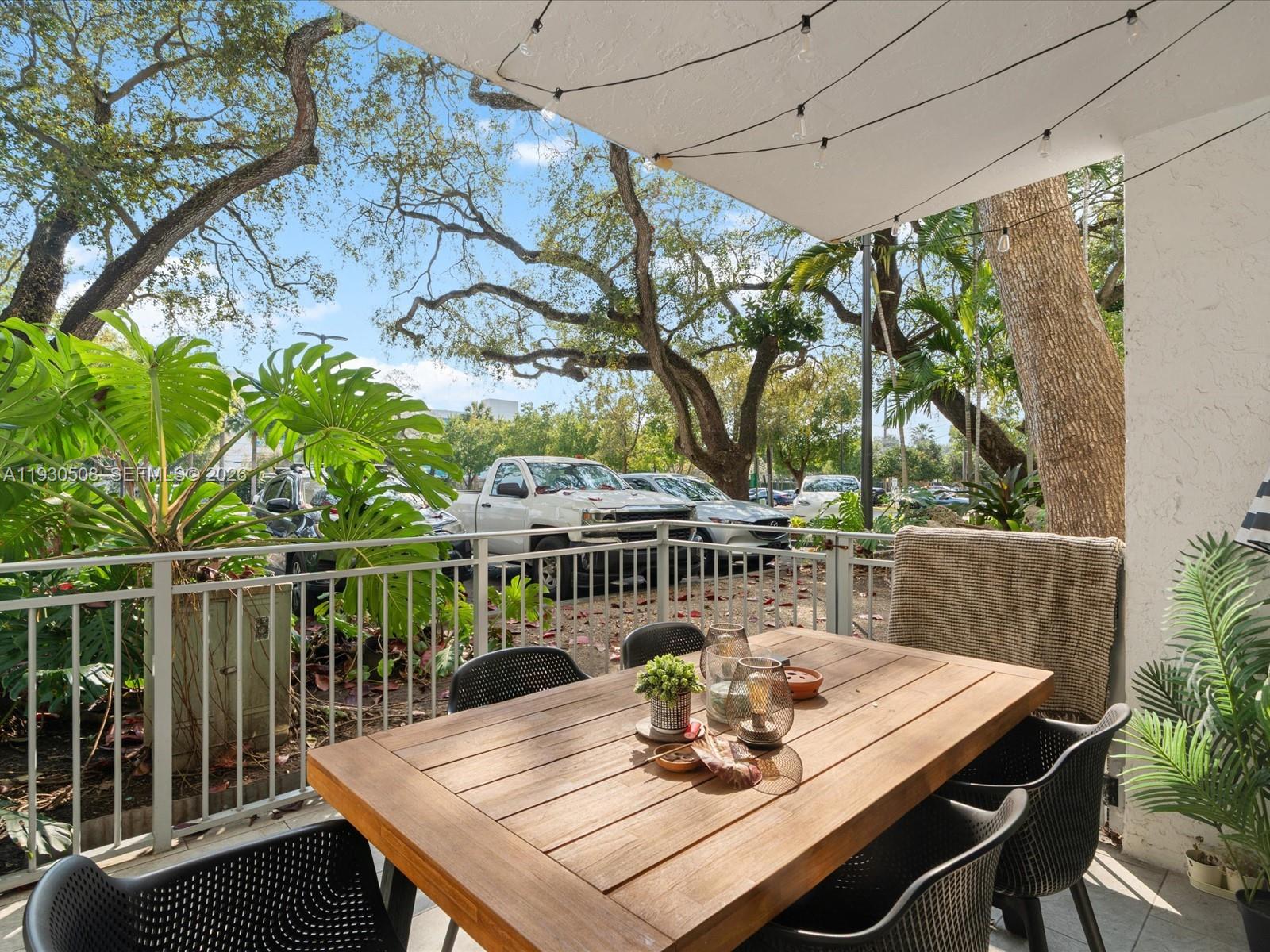 A patio features a wooden dining table with black chairs under string lights — 680 NE 64th St # A110, Miami FL 33138, MIAMI, FL