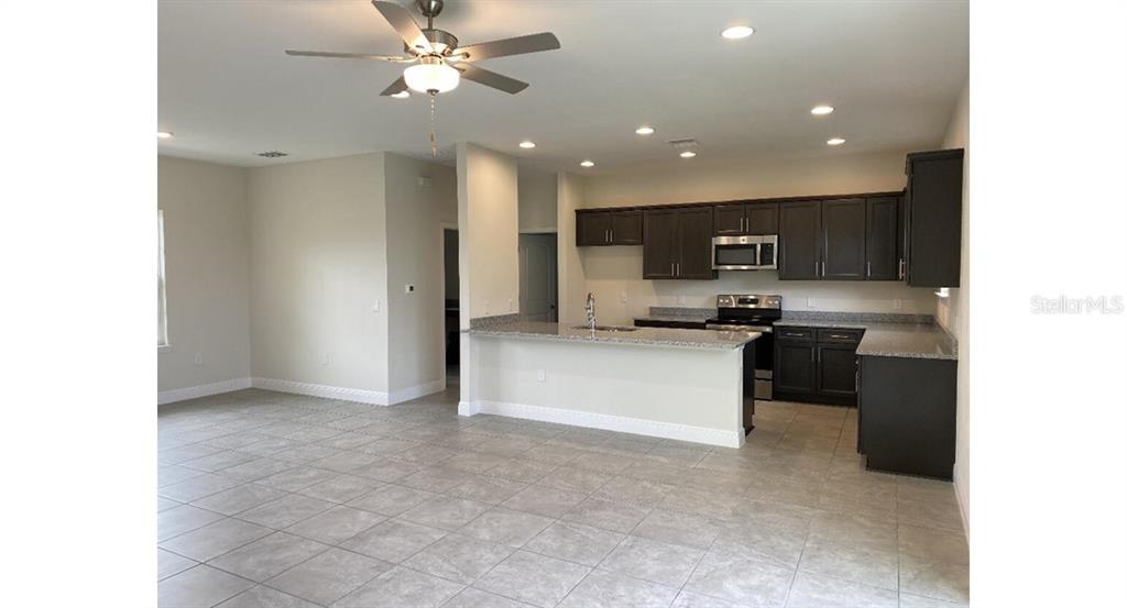 An open-concept kitchen features dark wood cabinets, granite countertops, and light tile flooring — 7050 BECKWITH AVENUE, NORTH PORT, FL